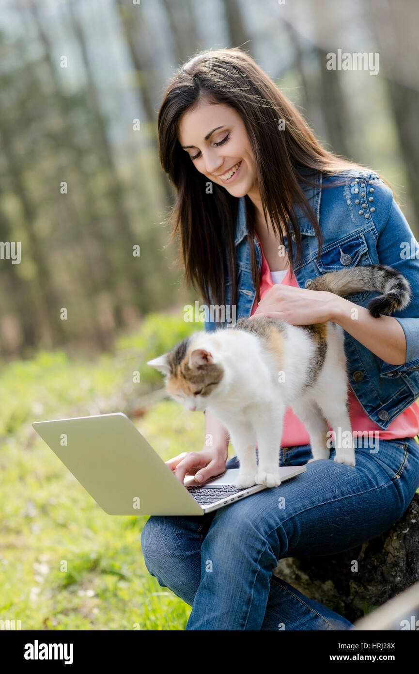 Junge Frau mit Katze sitzt mit Laptop in der Natur - woman with cat and laptop in nature Stock Photo