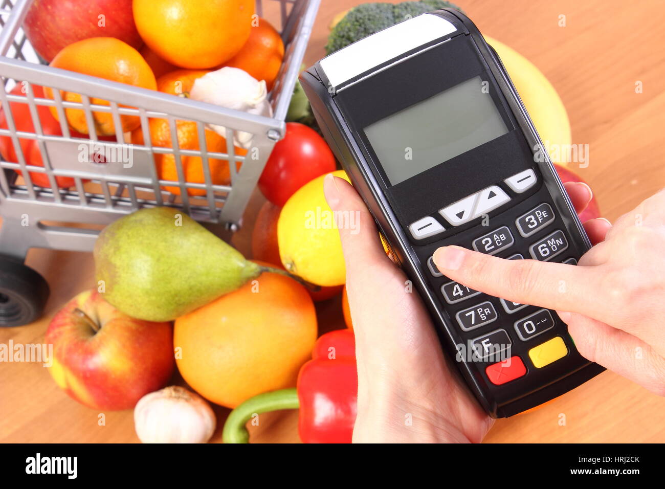 Hand of woman using payment terminal, enter personal identification number, credit card reader and fresh fruits and vegetables with plastic shopping c Stock Photo