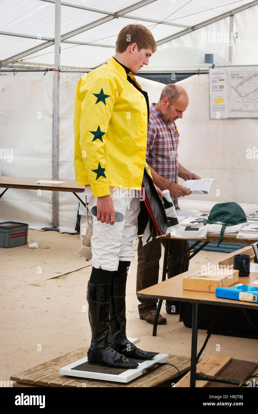 Jockey in a yellow shirt standing on weighing scale, being weighed