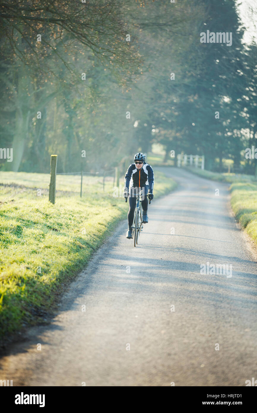 A cyclist pedalling along a country road, rear view. Stock Photo
