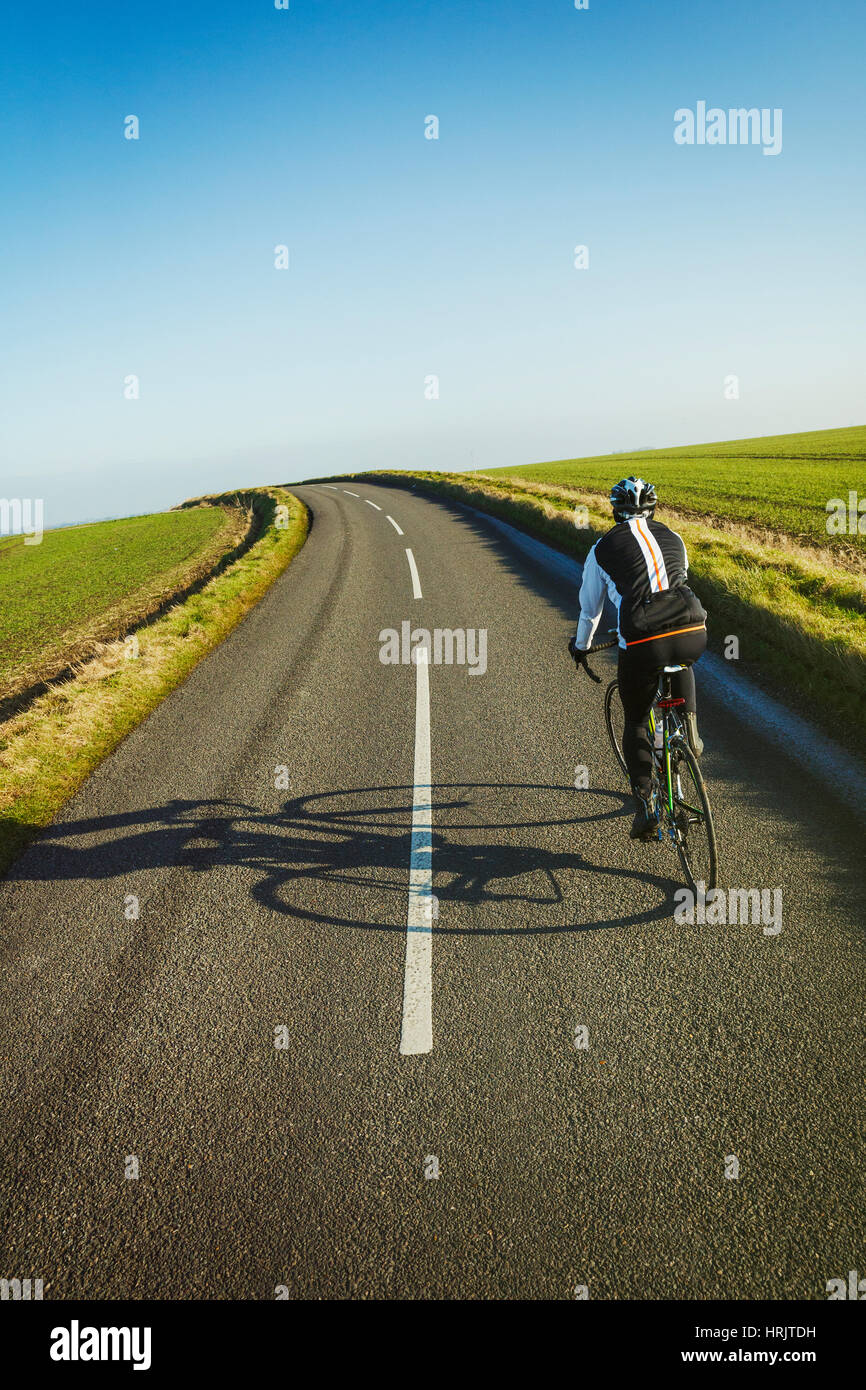 A cyclist pedalling along a country road, rear view. Stock Photo