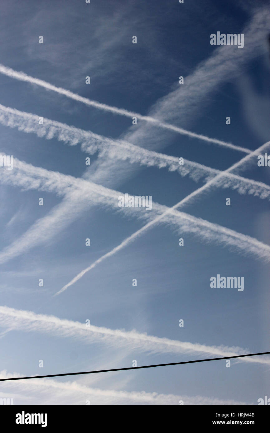 Multiple contrails crossing against blue sky and cirrus cloud and drifting in the wind, with an electricity power line at the base of the photo Stock Photo
