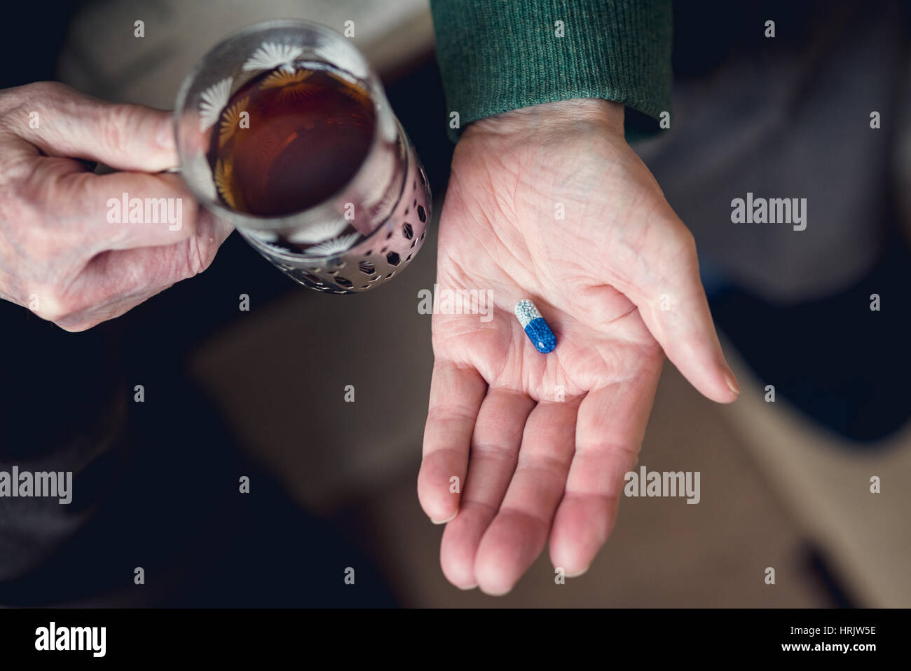 A senior man golding glass of hot tea and blue pill in other hand. Senility concept Stock Photo