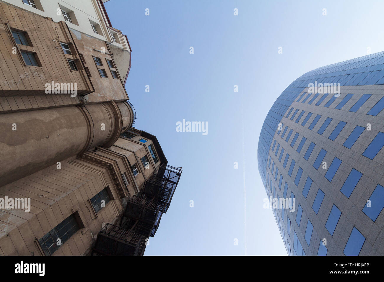 Side by side photo of classical building in front of modern glass office building with blue sky in between Stock Photo