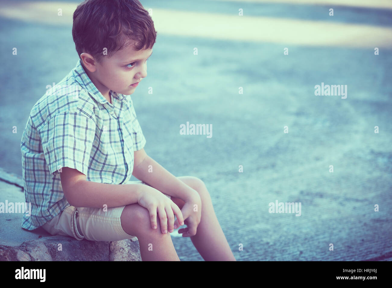 Portrait of sad little boy sitting on street at the day time Stock ...