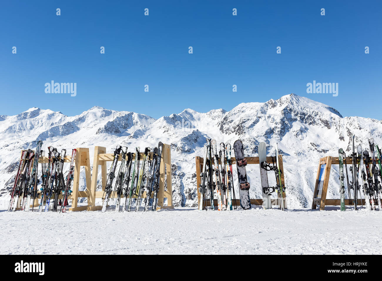 A line of skis and snowboards stored on racks outside a cafe on the slopes at Hochgurgl with the Otztal Alps in the background. All branding and logos Stock Photo