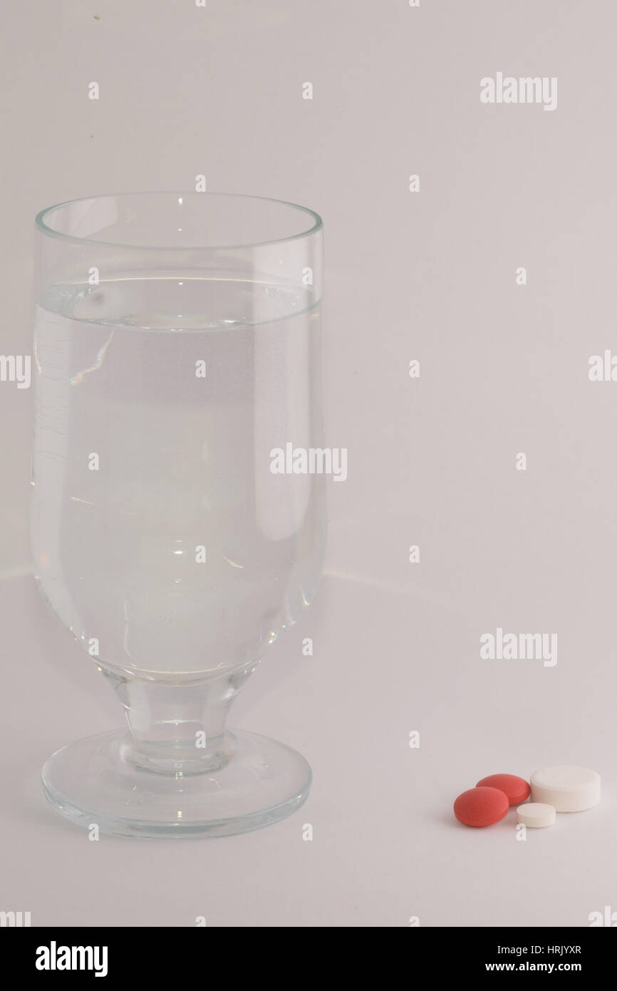 Glass of water beside red and white pills. Taking drugs concept. Stock Photo