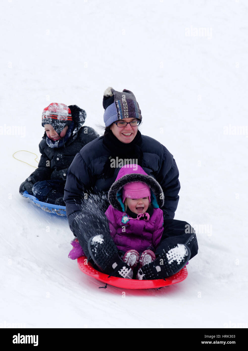 A laughing mum with her son and daughter sledging Stock Photo