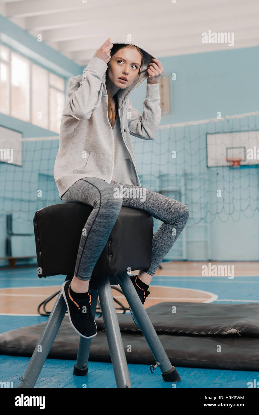 Young athletic woman in sportswear sitting on pommel horse in gym Stock Photo
