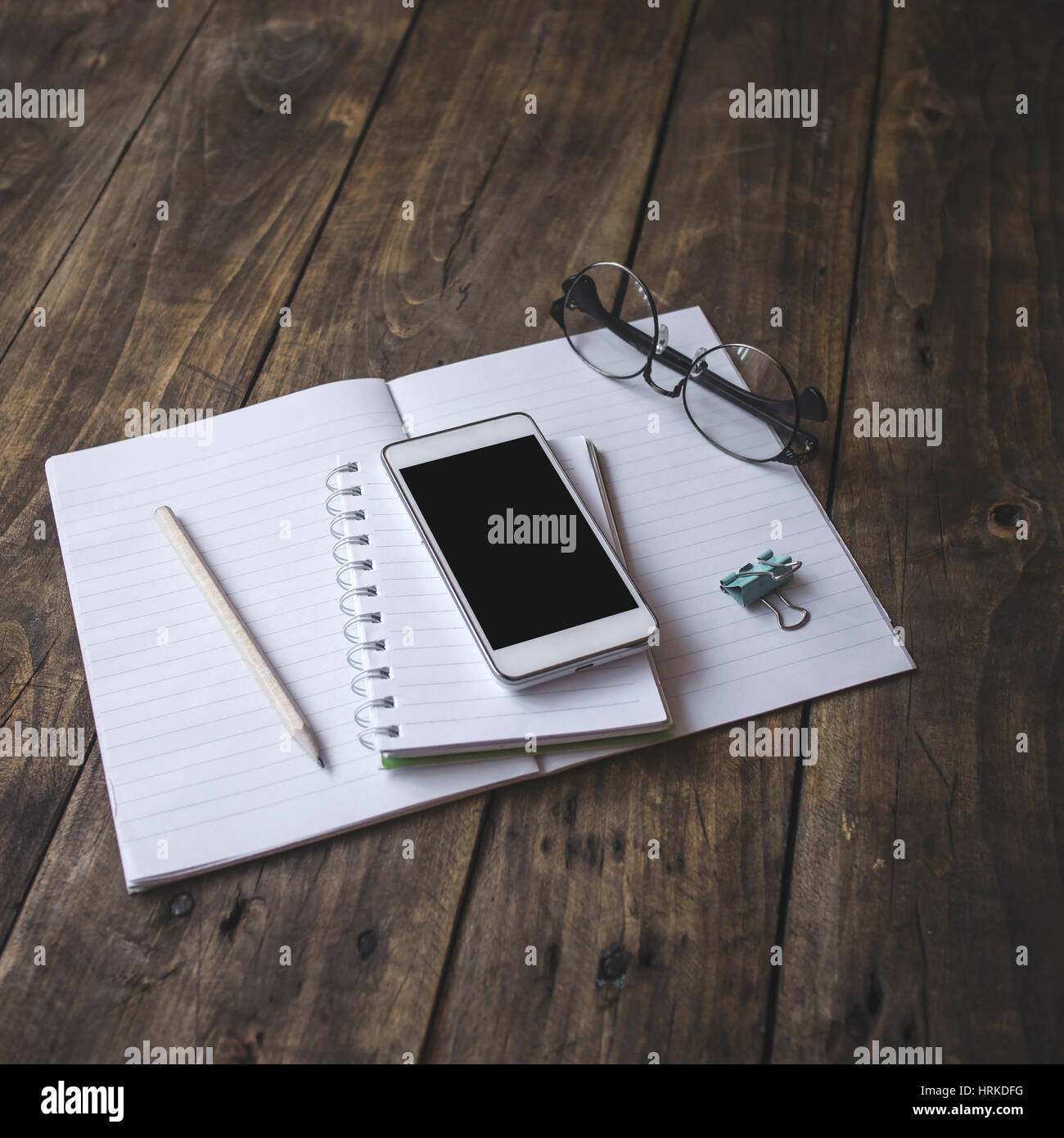 Home office tabletop: papers and notebooks, reading glasses, smart phone, pen on an old wooden board background. Vintage lifestyle. Stock Photo