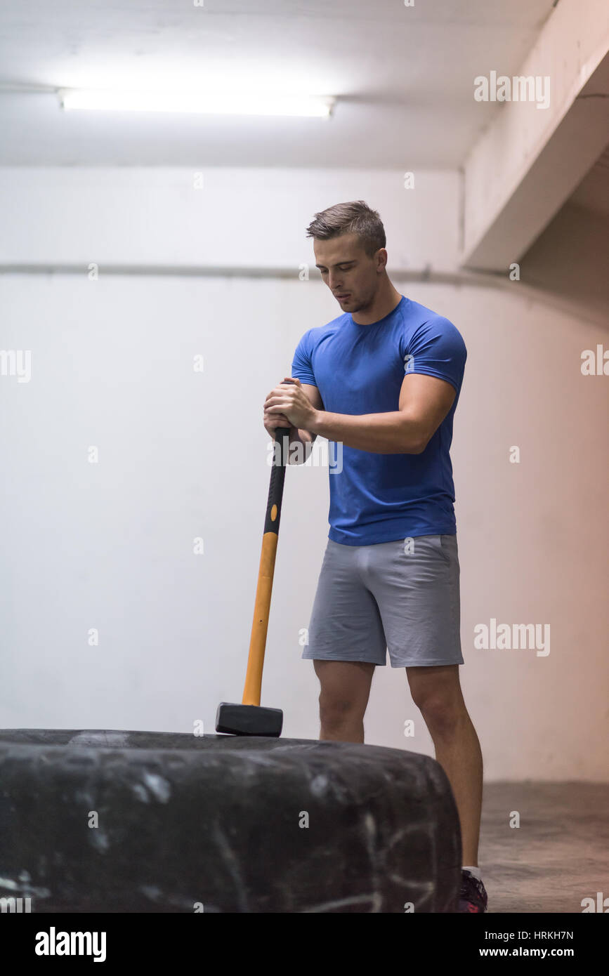 Sledgehammer Tire Hits young muscular man workout at gym with hammer