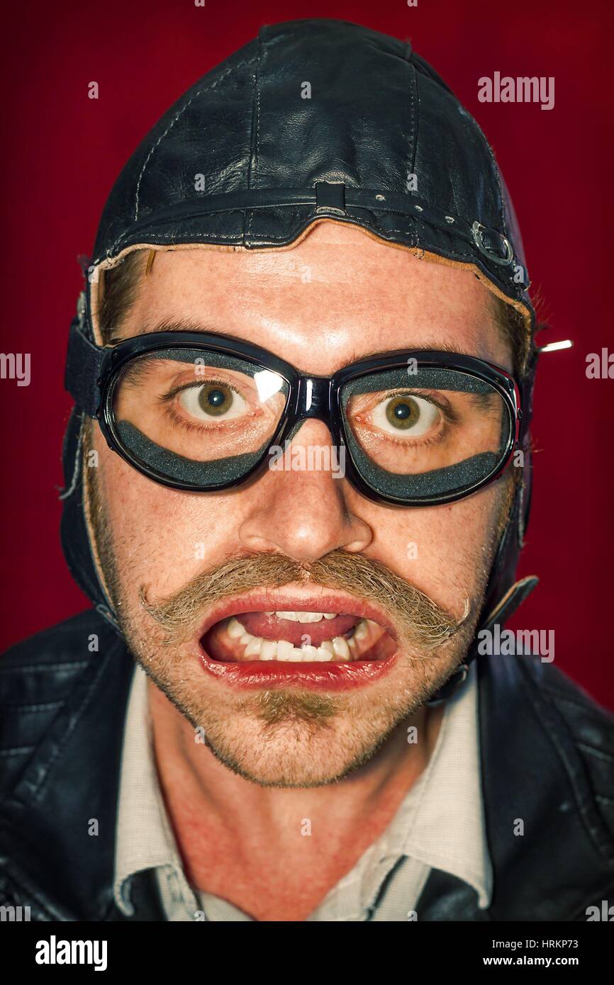 Man wearing aviator hat and goggles makes silly facial expression from