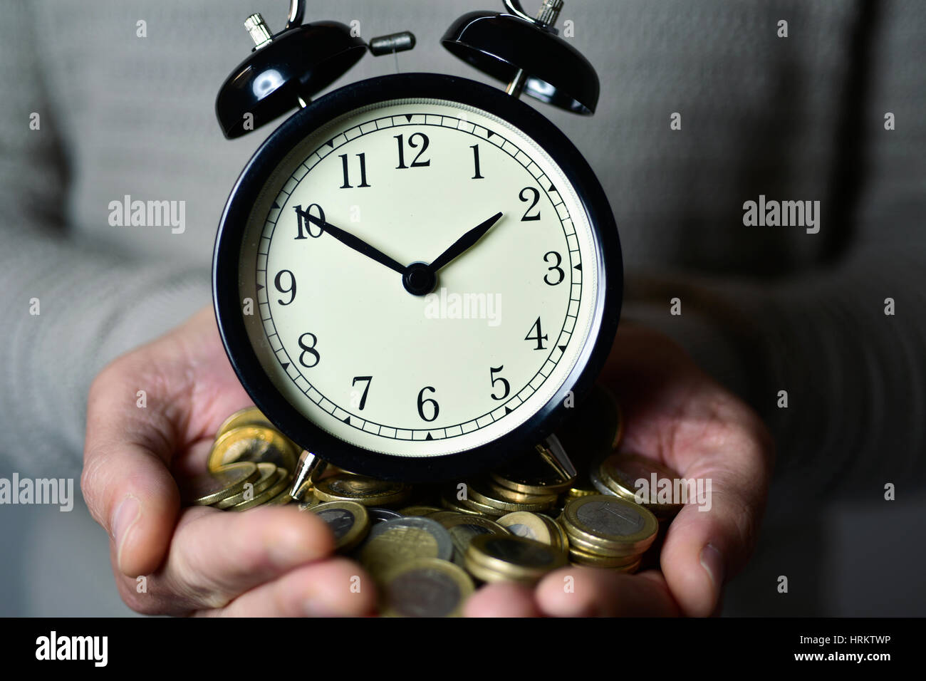 closeup of a young caucasian man with an alarm clock and many euro coins in his hands, depicting the idea that time is money Stock Photo