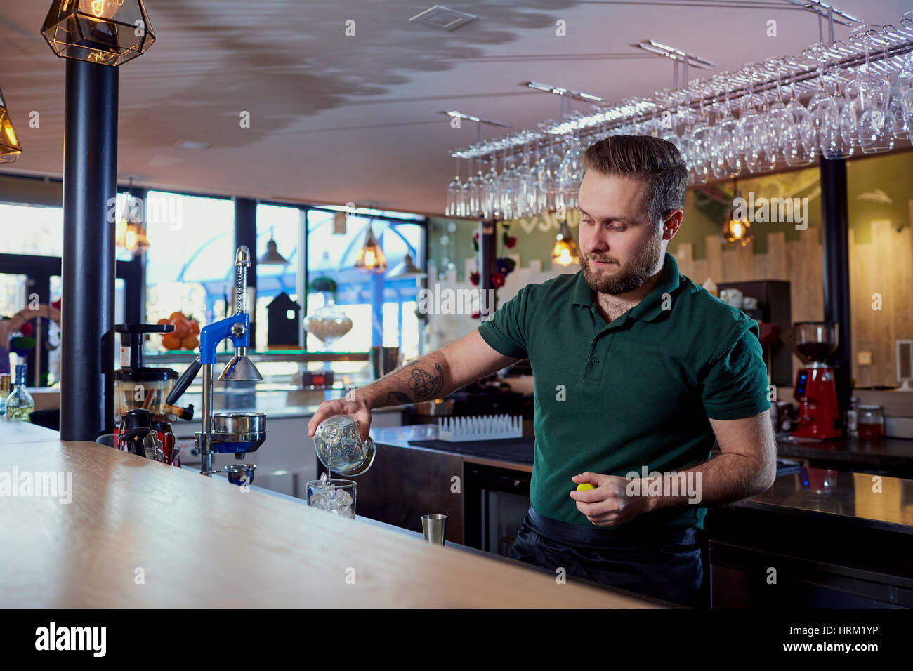 The bartender with beard behind bar pours a drink into  glass Stock Photo