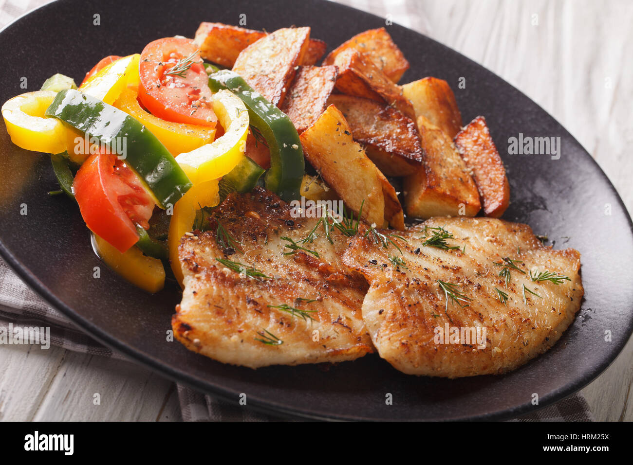 Grilled Tilapia fillet, fried potatoes, fresh salad on a plate closeup. horizontal Stock Photo