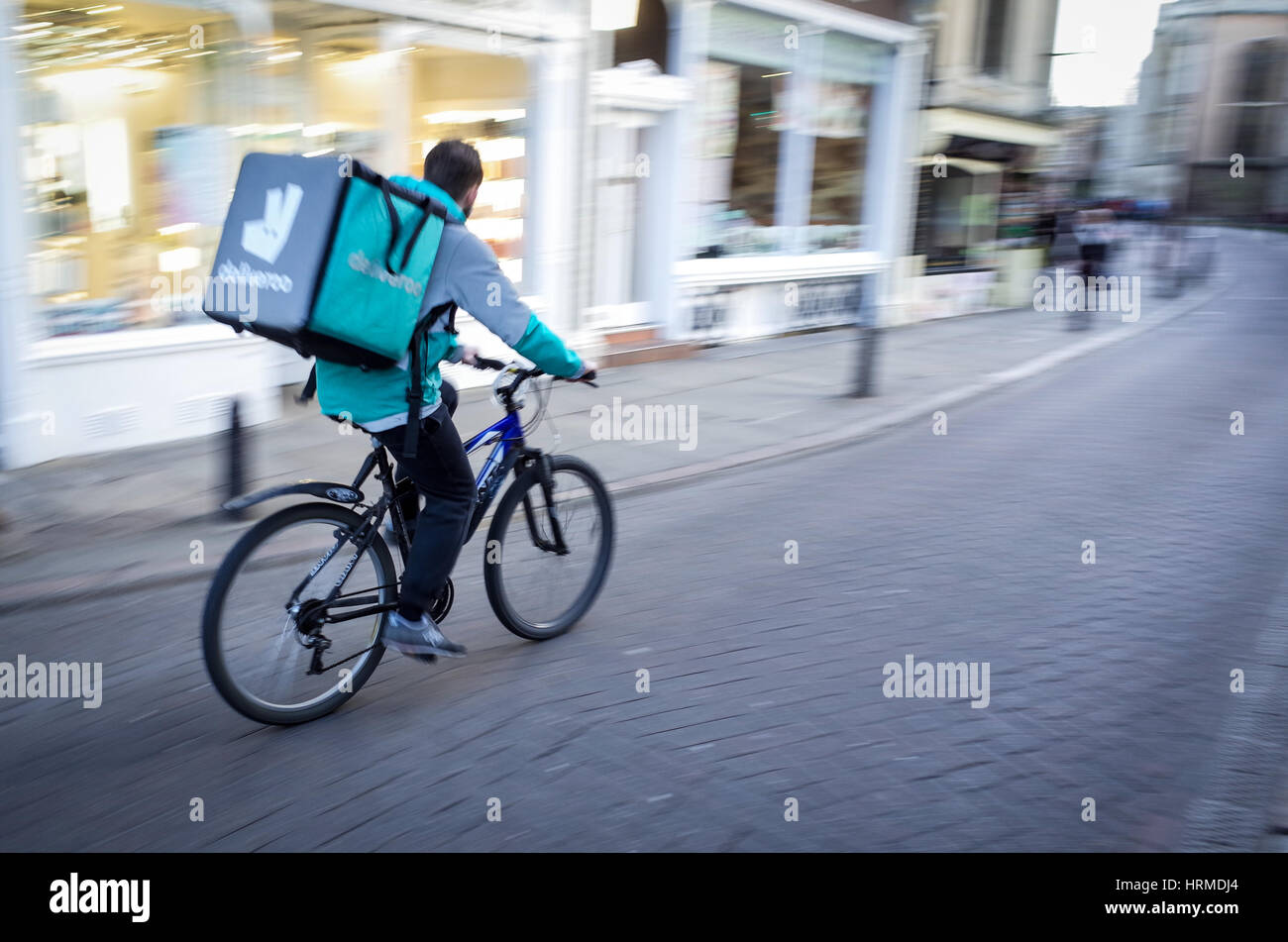 A Deliveroo food delivery courier rushes through central Cambridge UK Stock Photo