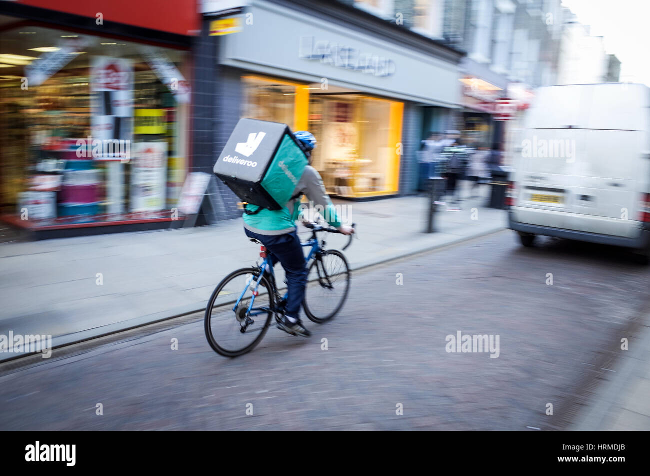A Deliveroo food delivery courier rushes through central Cambridge UK ...