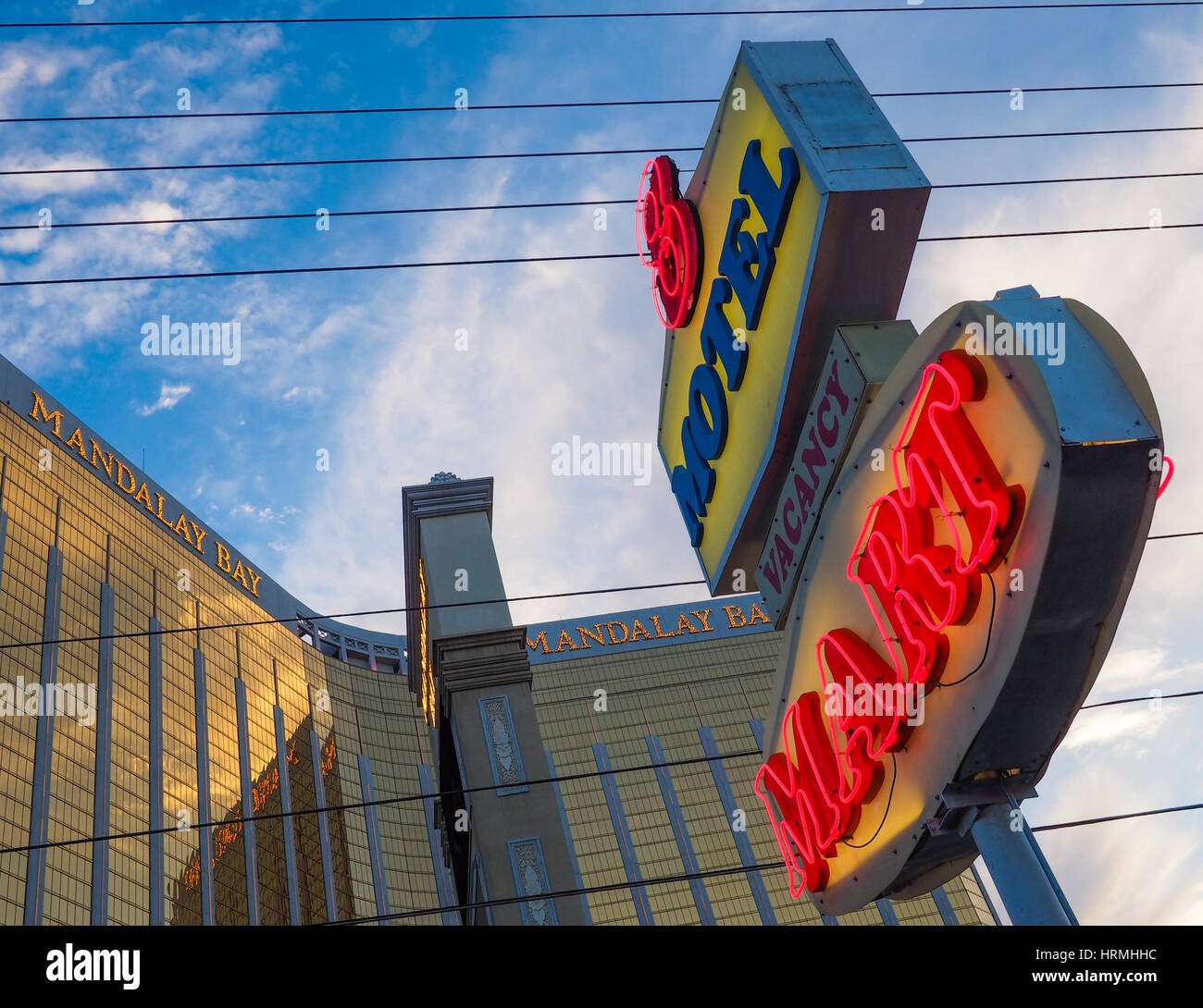 The illuminated neon sign of a budget motel in front of the facade of the Mandalay Bay luxury hotel and casino on the Las Vegas Strip. Stock Photo