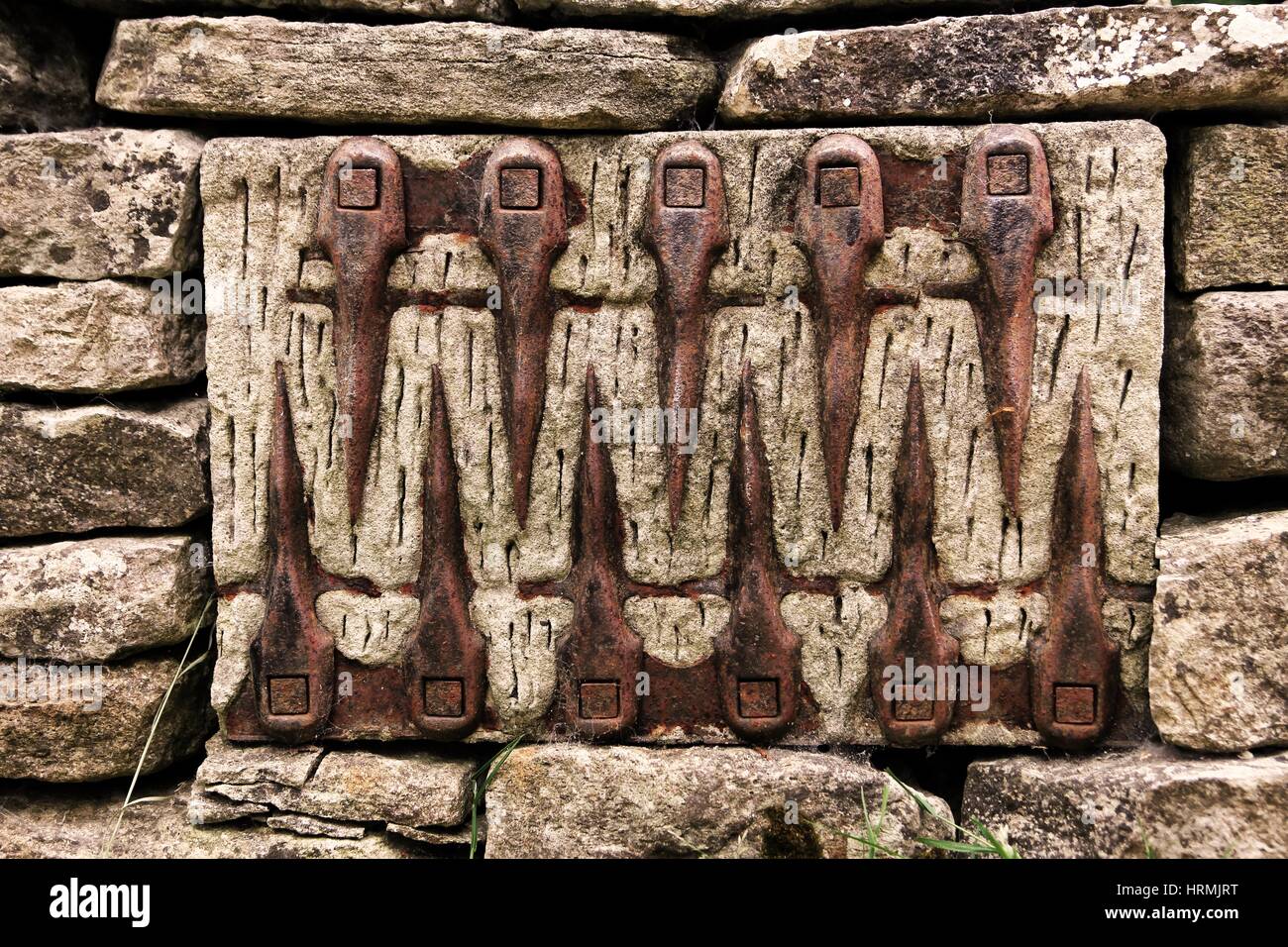 Unusual pattern of old farm tools set into a stone wall Stock Photo