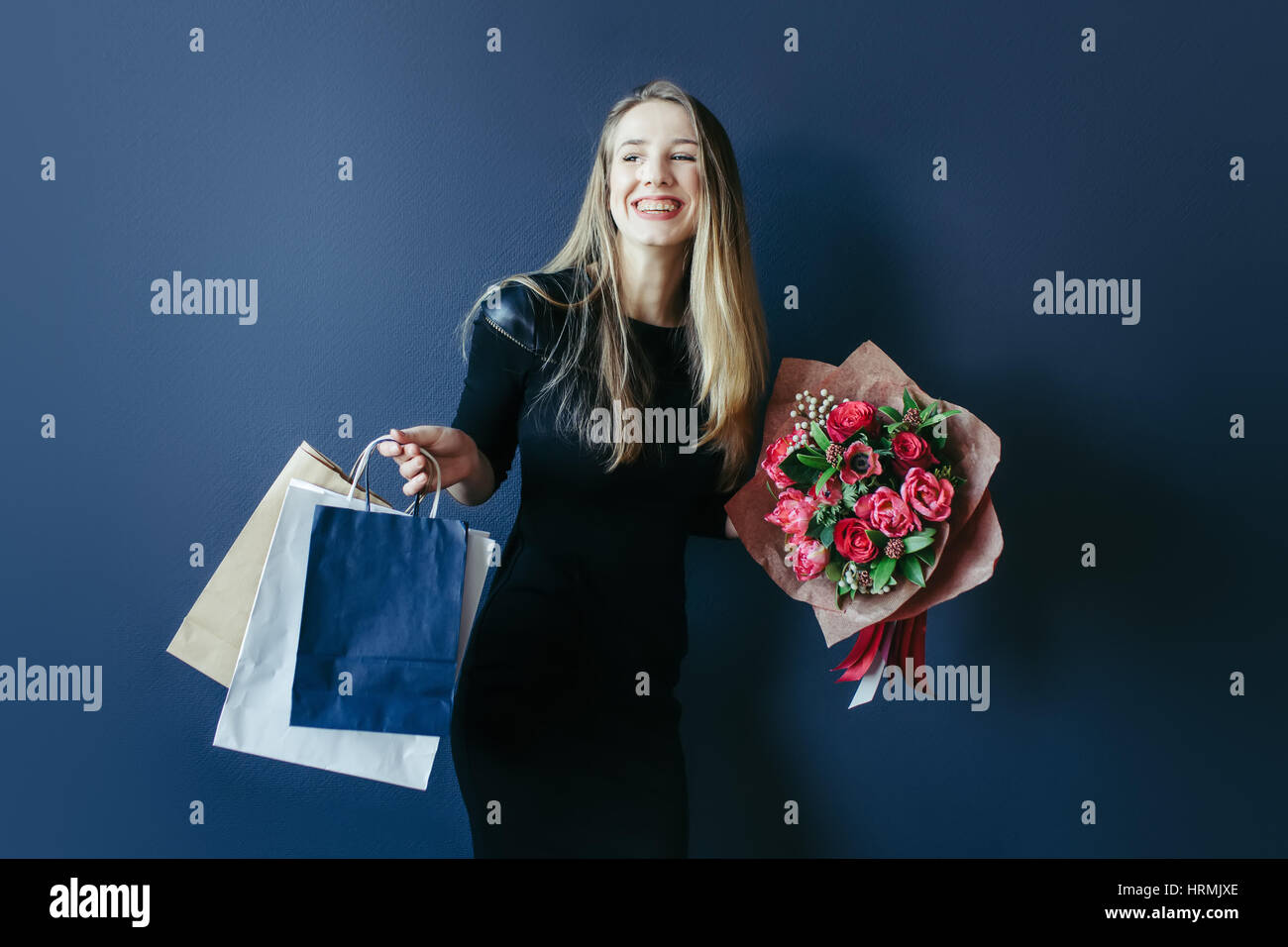 Girlfriend with bouquet of red tulips and gift in paper packages. Studio. Stock Photo