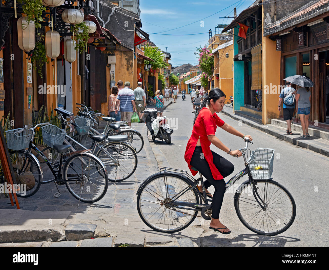 Young Vietnamese woman in red ao dai dress riding bicycle. Hoi An Ancient Town, Quang Nam Province, Vietnam. Stock Photo