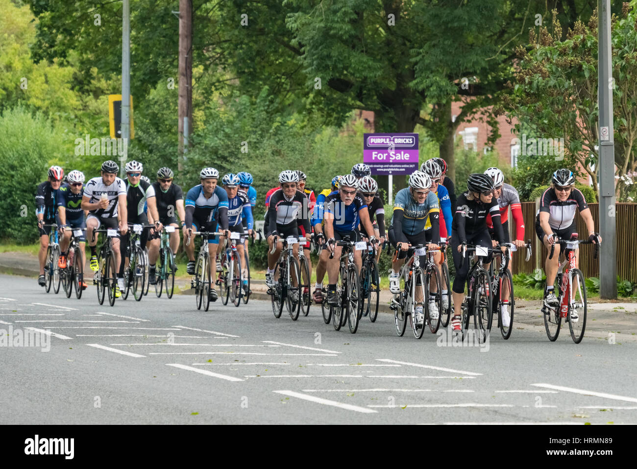 Large group of cyclists on the Rise Above sportive riding through Pulford near Chester Stock Photo