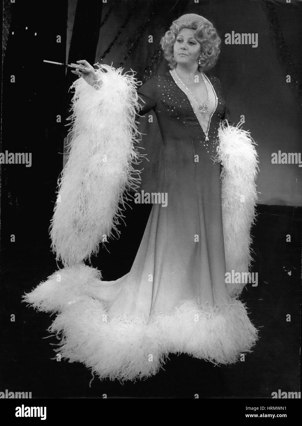 Jan. 11, 1974 - Bernard Gavoty asked Regine Crespin to be his guest for the traditional get-togethers held at the Royal Palace during the month of January. She will be surrounded by Jacques Martin, Madame Soleil, and Raymond Olivier. Regine Crepin is pictured here wearing a 1930s gown, a white boa, a blonde wig, and carrying an immense cigarette holder. (Credit Image: © Keystone Press Agency/Keystone USA via ZUMAPRESS.com) Stock Photo