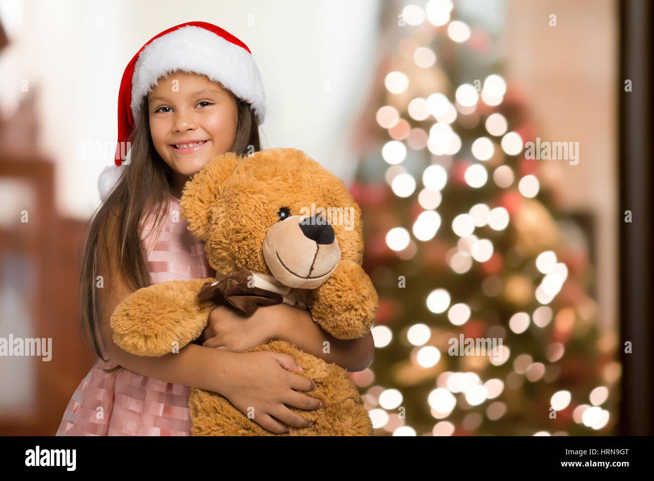Little pretty girl hugging bear against of Christmas tree Stock Photo ...