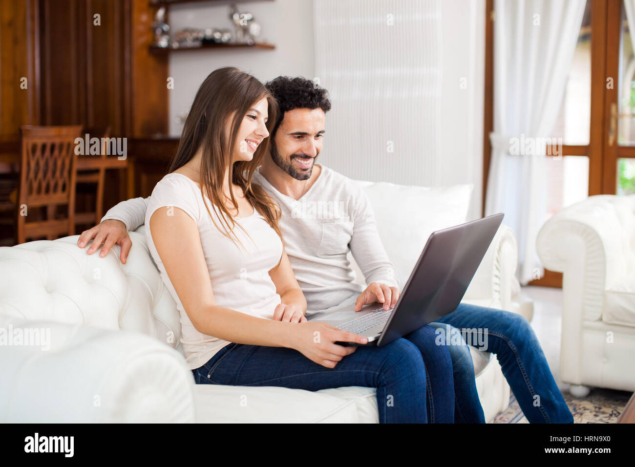 Happy couple using a laptop on the sofa Stock Photo - Alamy