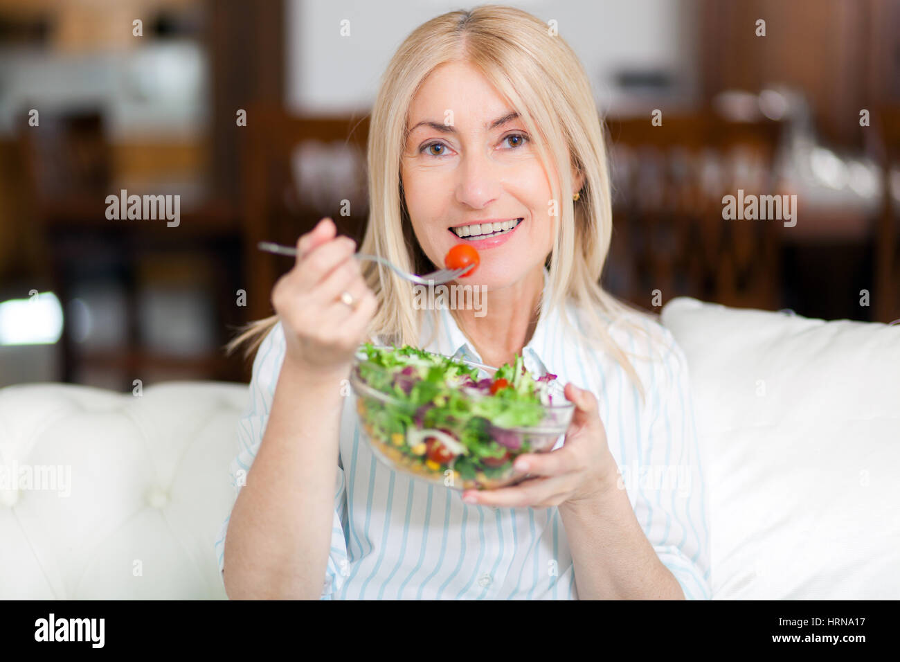 Mature woman eating a healthy salad on her sofa Stock Photo Alamy