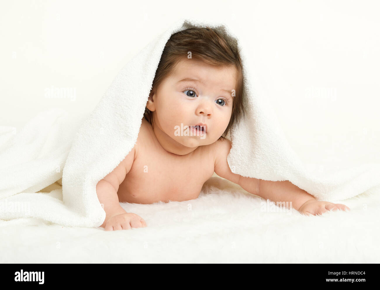 Baby lie on white towel. Child in bed. The head is covered with a