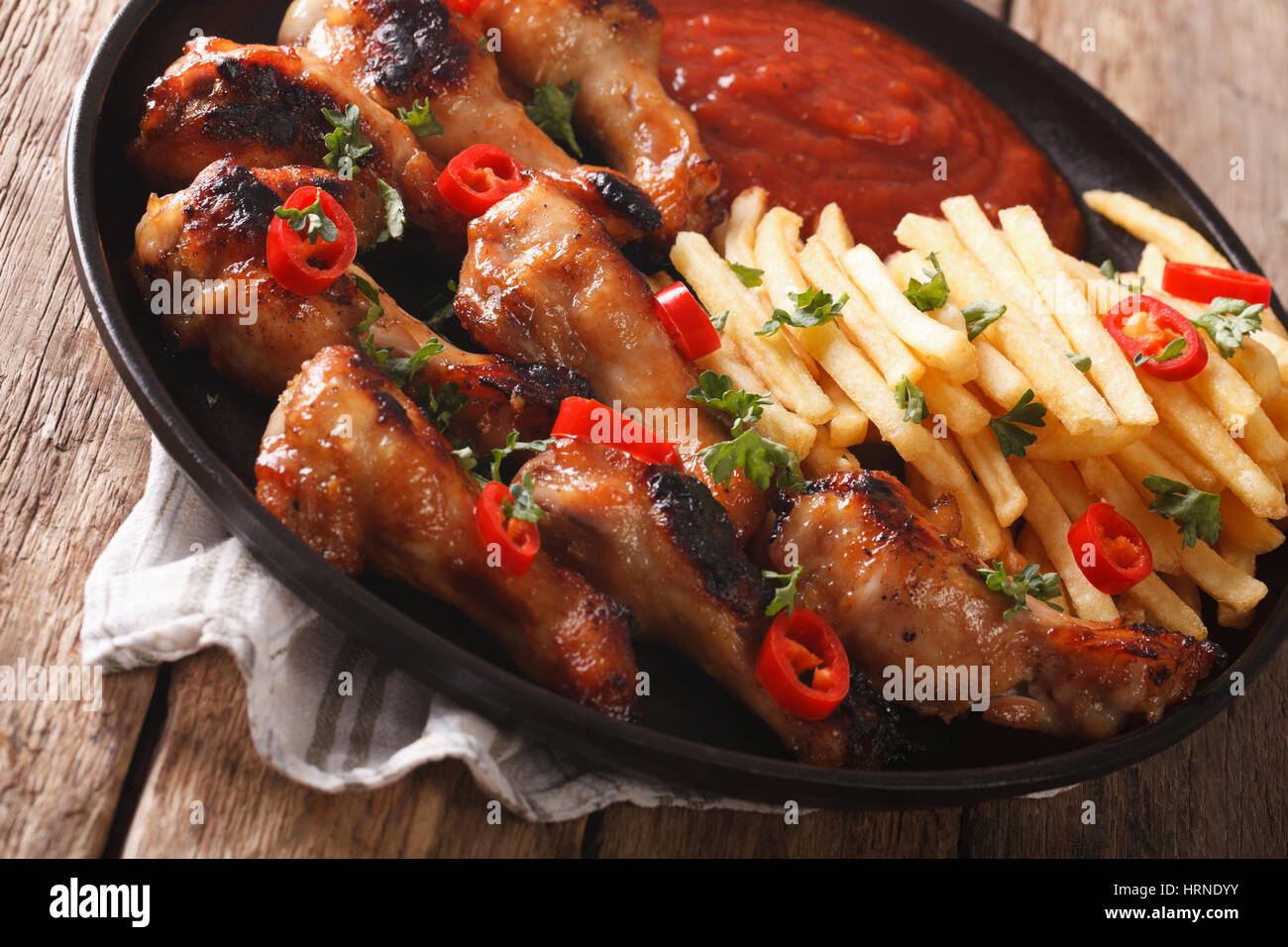 Spicy BBQ chicken wings with french fries and sauce on a plate close-up. horizontal Stock Photo