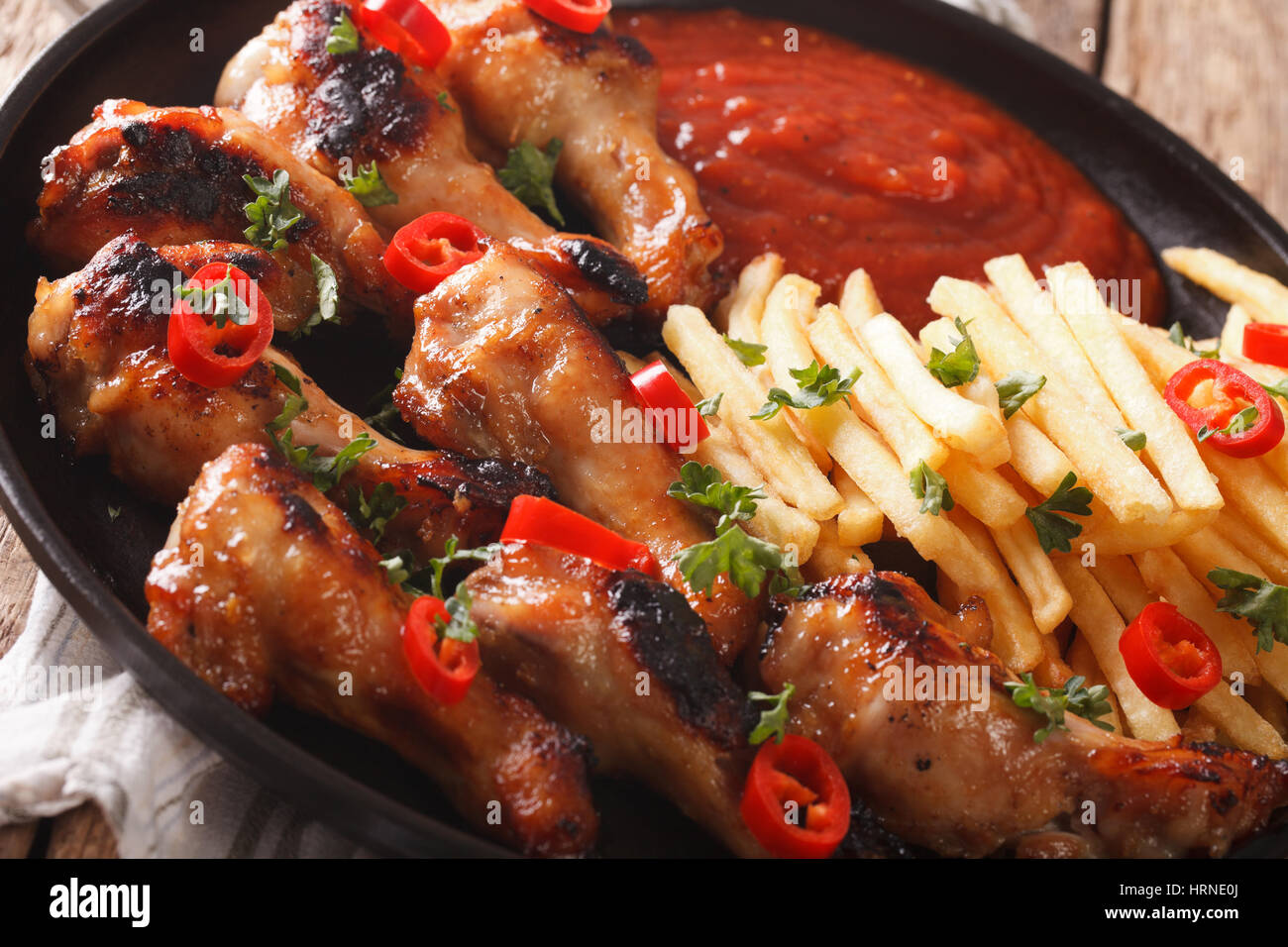 Delicious barbecue chicken wings with french fries and ketchup on a plate close-up. horizontal Stock Photo