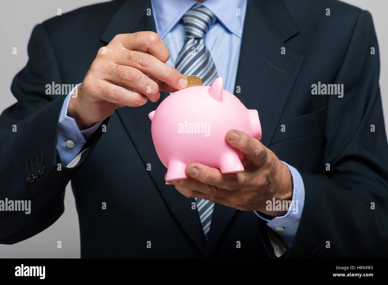 Businessman's hand putting money in a piggy bank Stock Photo - Alamy