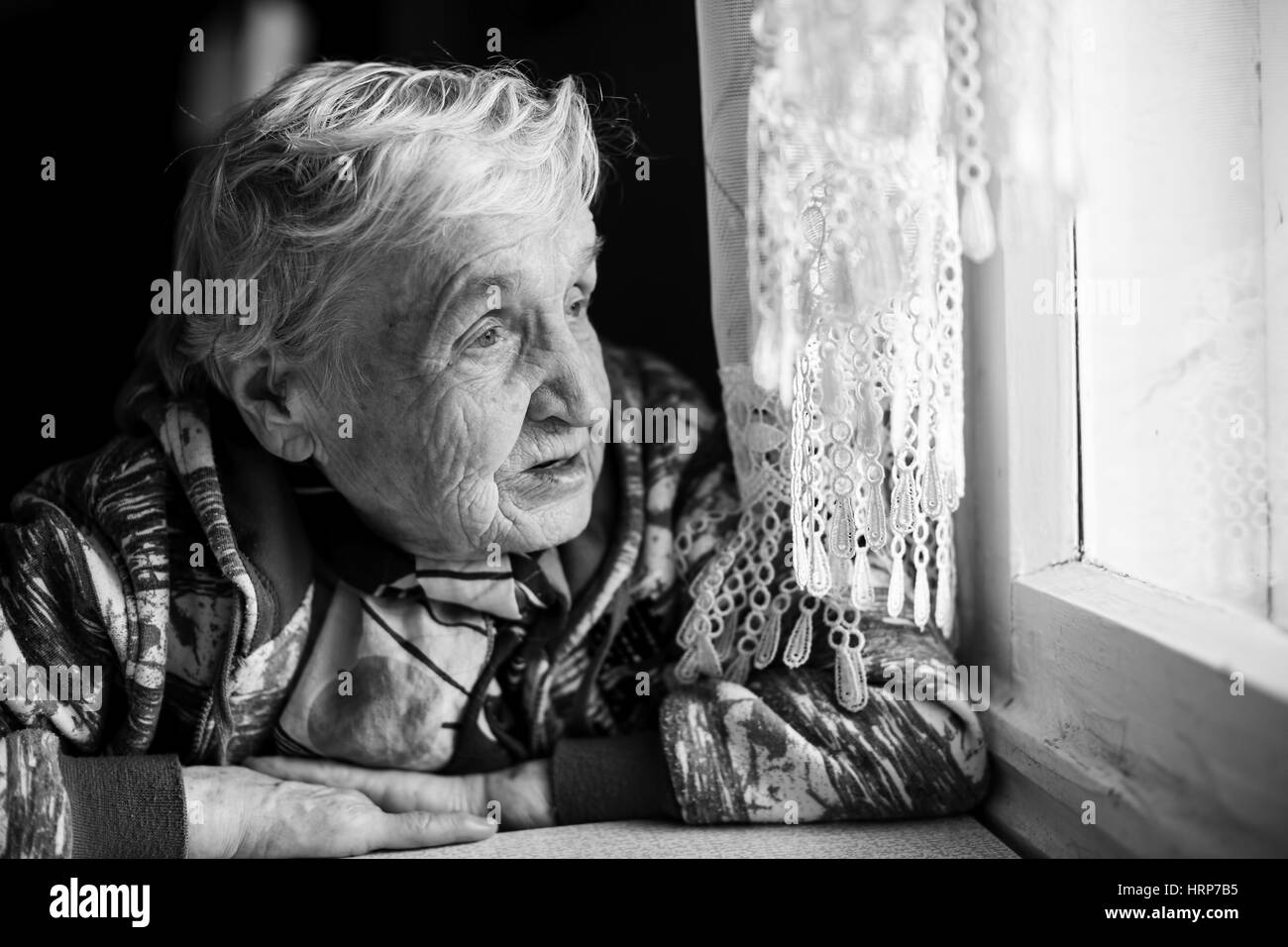 Black-and-white photo of an elderly woman near the window. Stock Photo