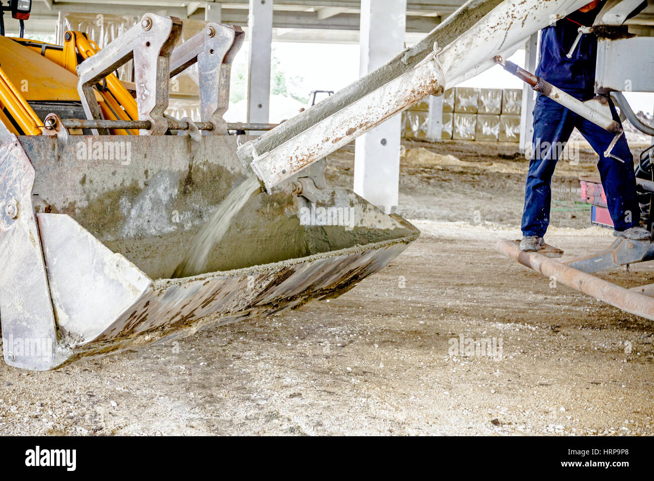 Concrete mixer truck is pouring fresh concrete into excavator bucket at
