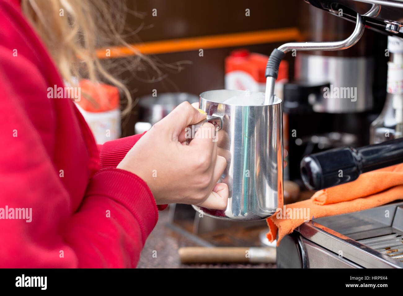 Young attractive blod woman frothing milk in silver container for cappucino. Food truck retail seller in Wroclaw, Poland Stock Photo