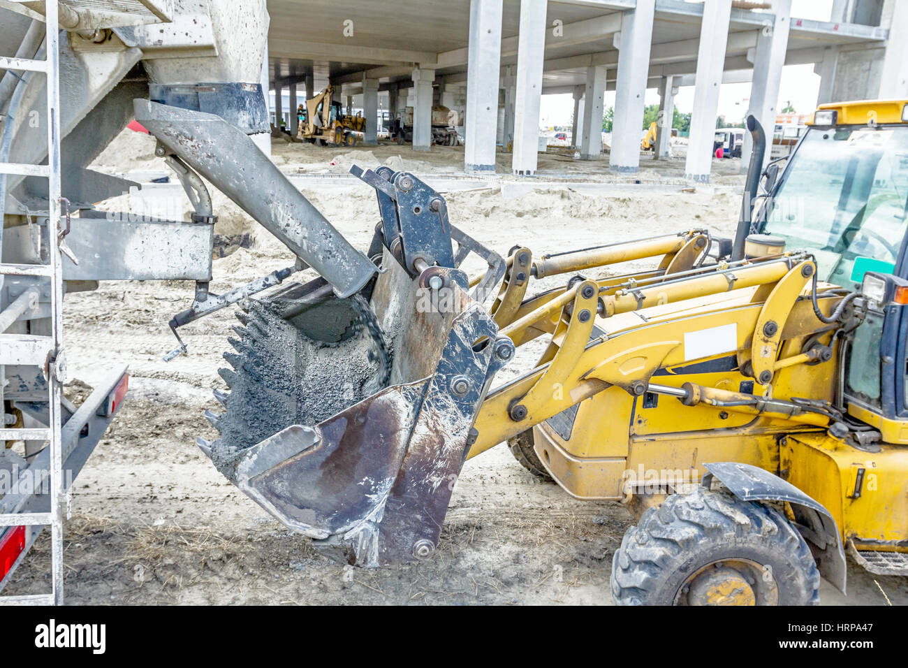 Concrete mixer truck is pouring fresh concrete into excavator bucket at