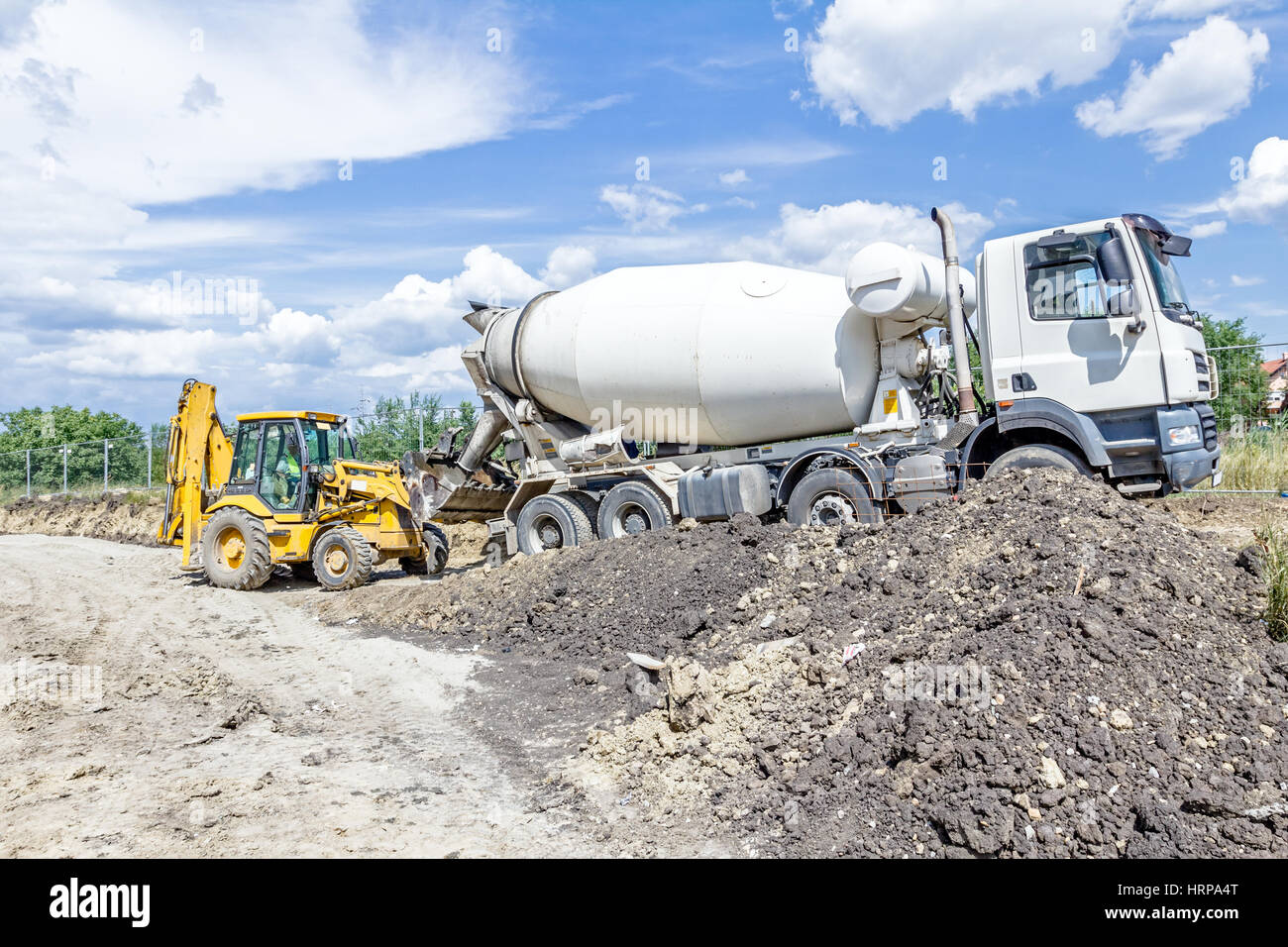 Concrete mixer truck is pouring fresh concrete into excavator bucket at