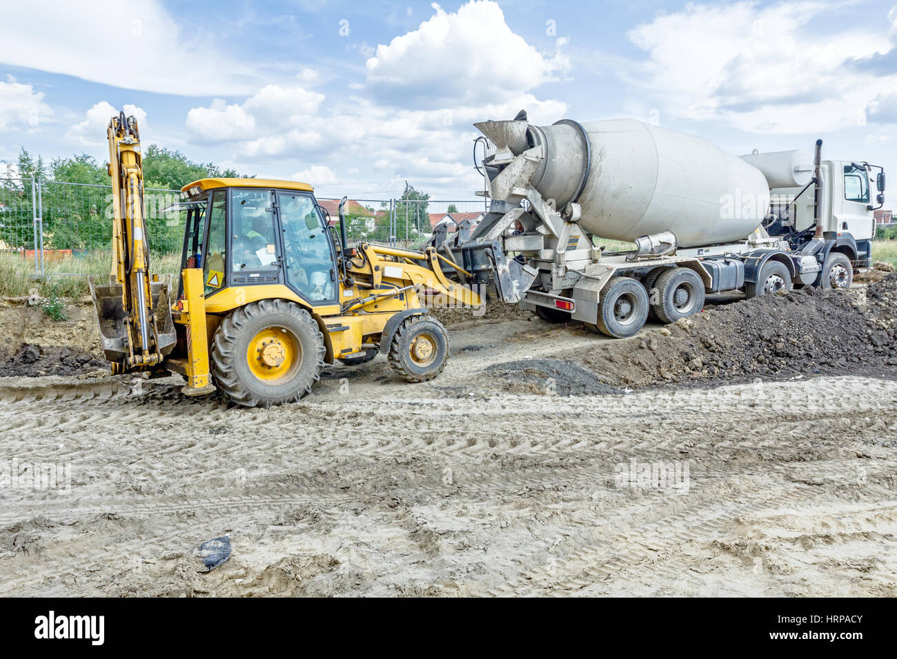 Concrete mixer truck is pouring fresh concrete into excavator bucket at