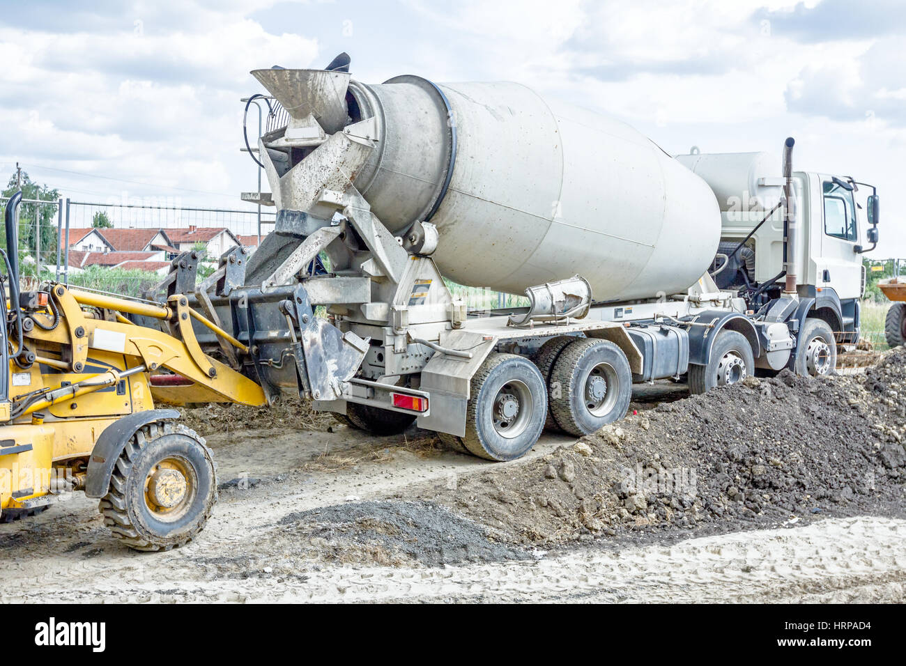 Concrete mixer truck is pouring fresh concrete into excavator bucket at