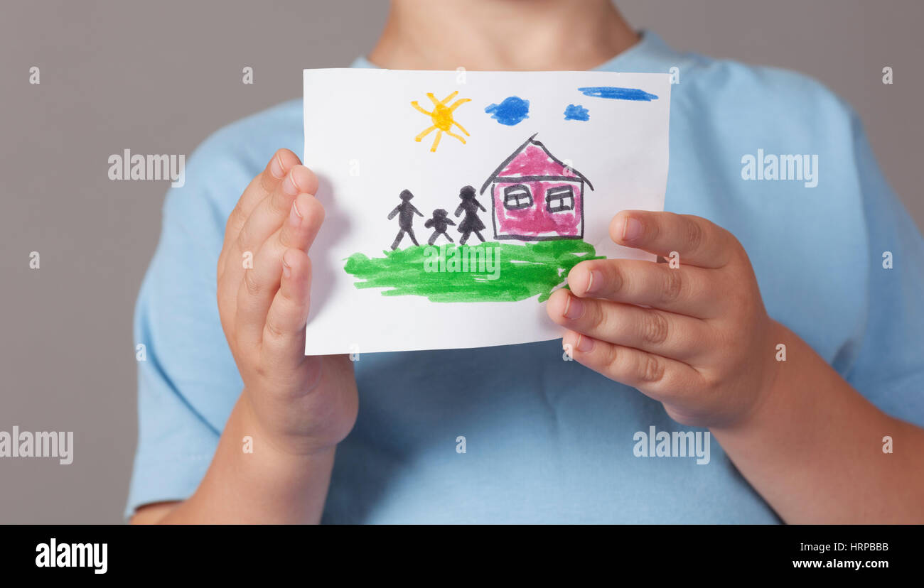 Child holds a drawn house with family in his hands. Close up. Stock Photo