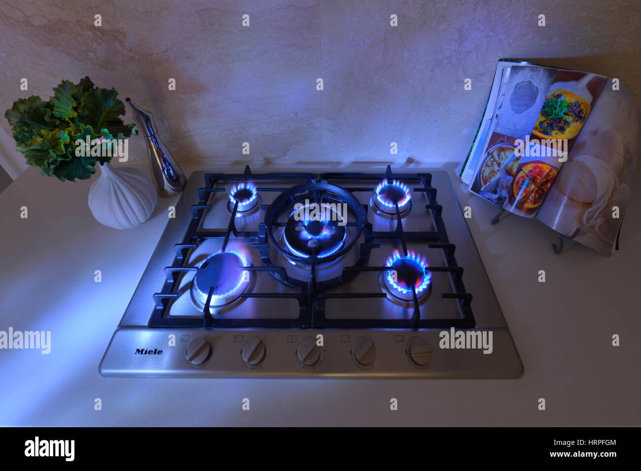 Close up view of burners alight on a five burner hob with blue ambient lighting. Stock Photo
