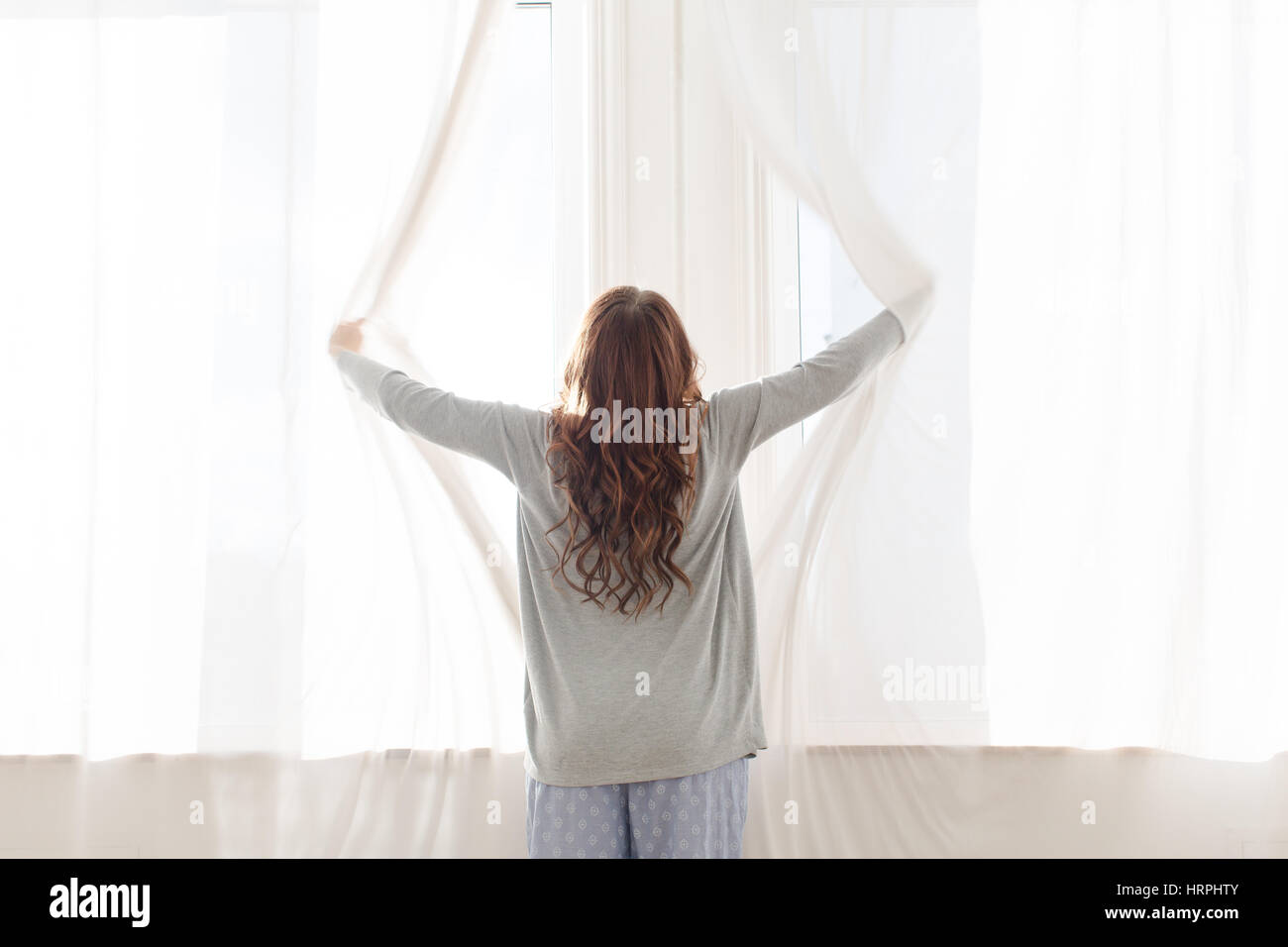 Female opens the curtains early in the morning, back view Stock Photo