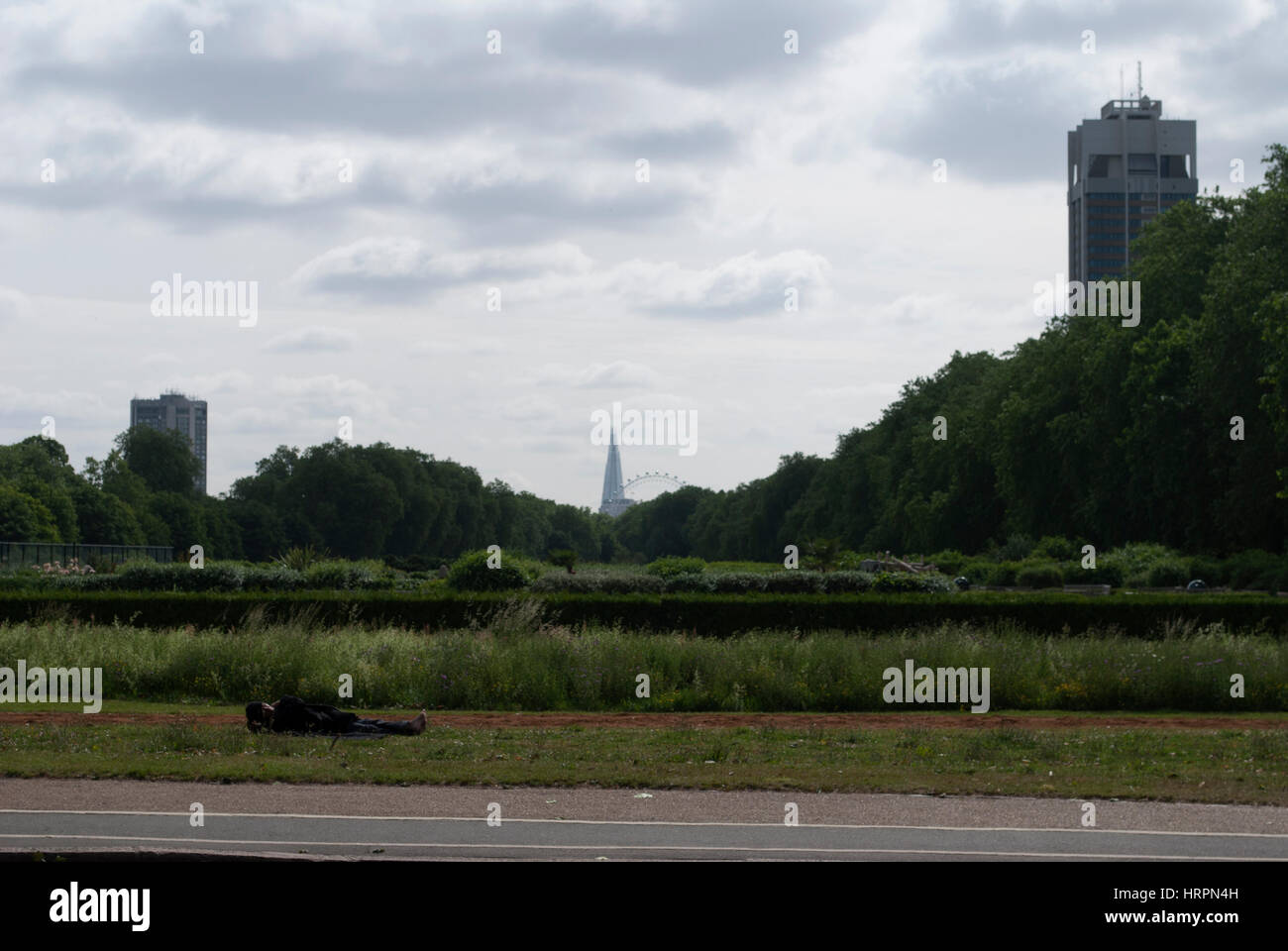 Homeless man sleeping on grass at the edge of Hyde Park with The Shard in the distance Stock Photo