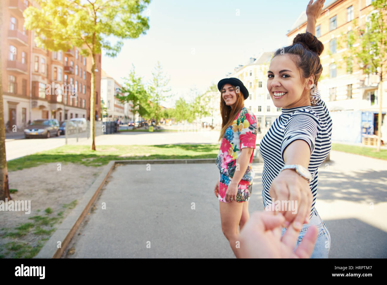 Two beautiful sisters holding hand of photographer from first person perspective in urban scene Stock Photo