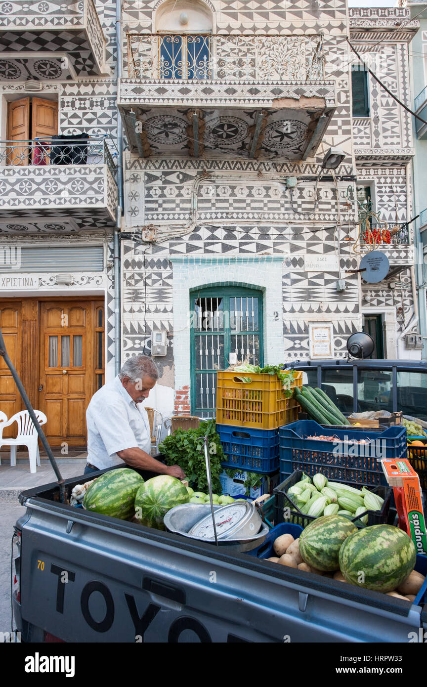A wondering greengrocer selling vegetables and fruits from the back of his pick up track parked in a street in Pyrgi, Chios. In the background a typic Stock Photo