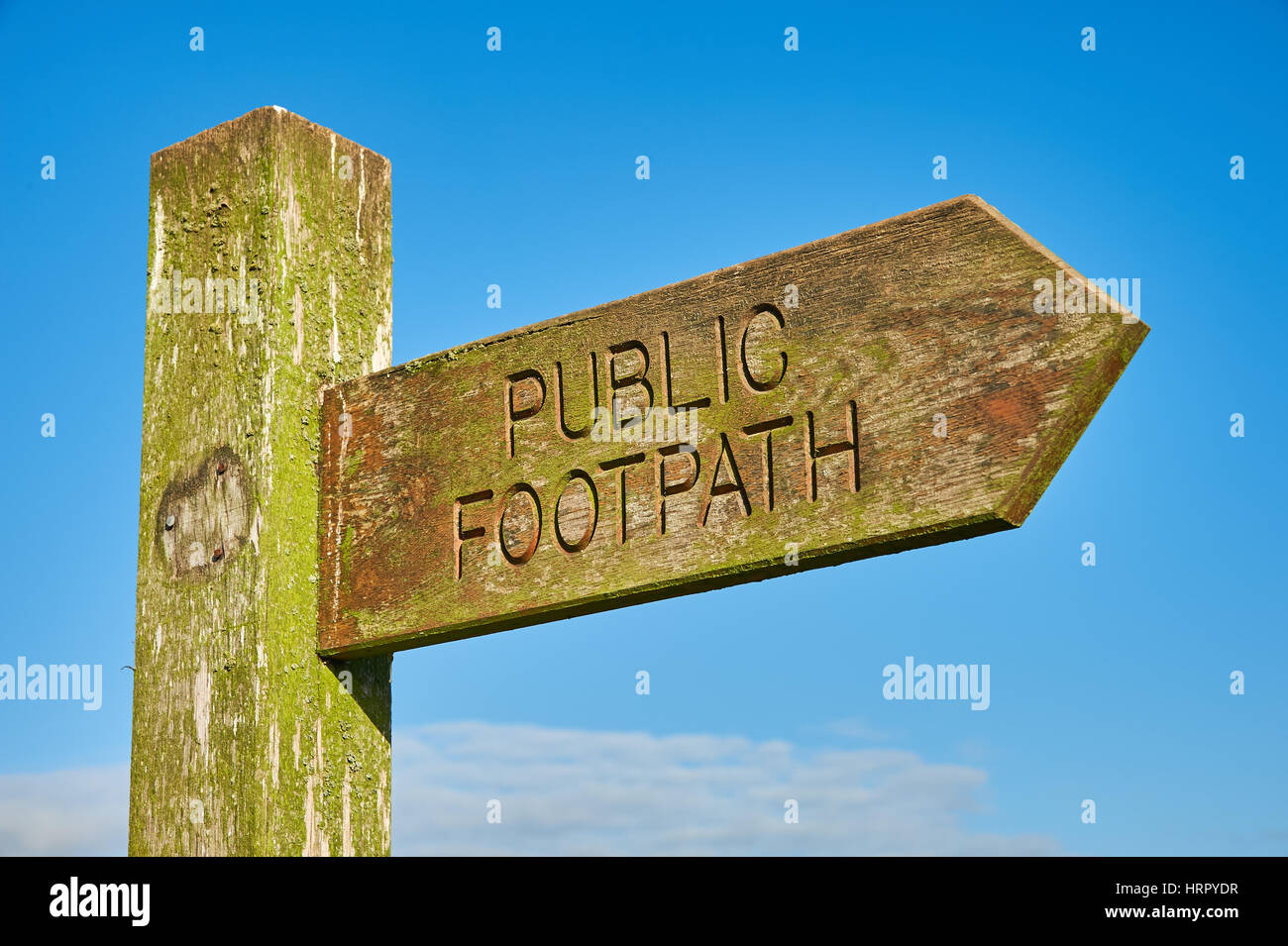 A timber fingerpost sign indicating a public footpath right of way, against a blue sky. Stock Photo