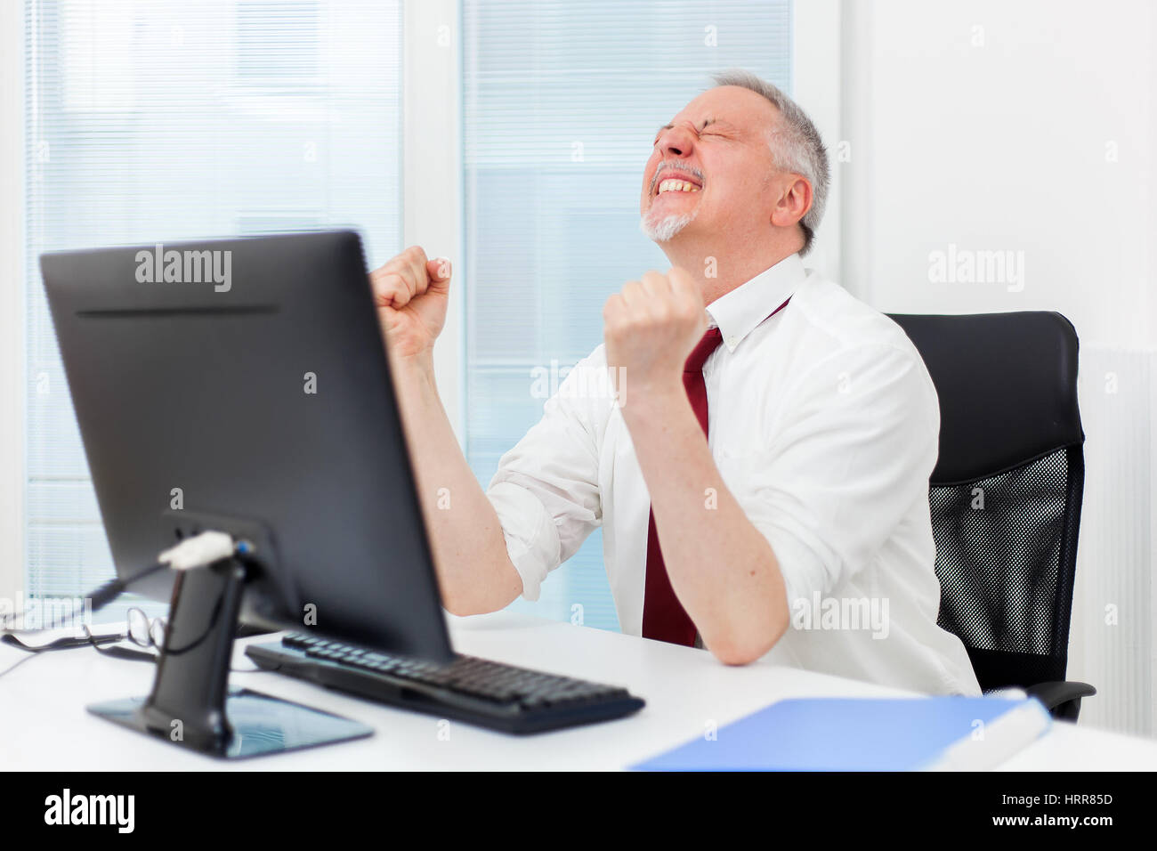 Mature businessman raising arms in front of his pc Stock Photo - Alamy
