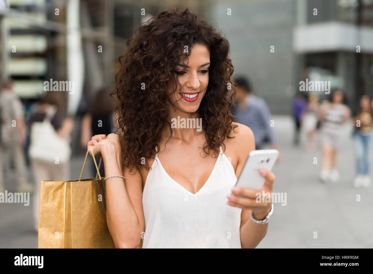 Smiling woman holding shopping bags while using her mobile phone Stock Photo